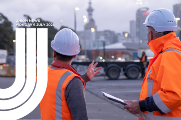 Two workers in orange hi-vis vests and white hard hats at an industrial port site, with the Auckland city skyline in the background. Text reads "Union News, Monday 6 July 2026".