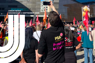 Union News graphic featuring a crowd of union members at an outdoor rally, holding flags and placards. In the foreground, people wear black PSA T-shirts reading 'Proud to be Union' and 'Stand together for public services'. One person holds a phone overhead to film the crowd.