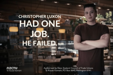 Still from an NZCTU campaign advertisement. Large white text over a dimly lit café interior reads “Christopher Luxon had one job. He failed.” On the right, a young man in a dark red T-shirt stands with his arms folded, looking at the camera. The NZCTU Te Kauae Kaimahi logo sits in the bottom left, with an authorisation statement.